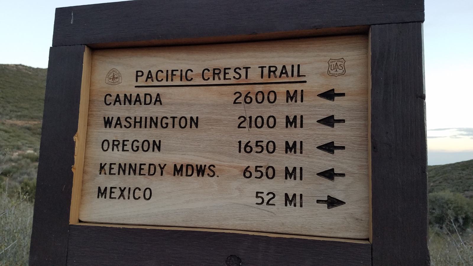 Wooden trail sign: Canada 2,600 miles, Washington 2,100, Oregon 1,650 and Kennedy Meadows 650 point left; Mexico 52 points right.